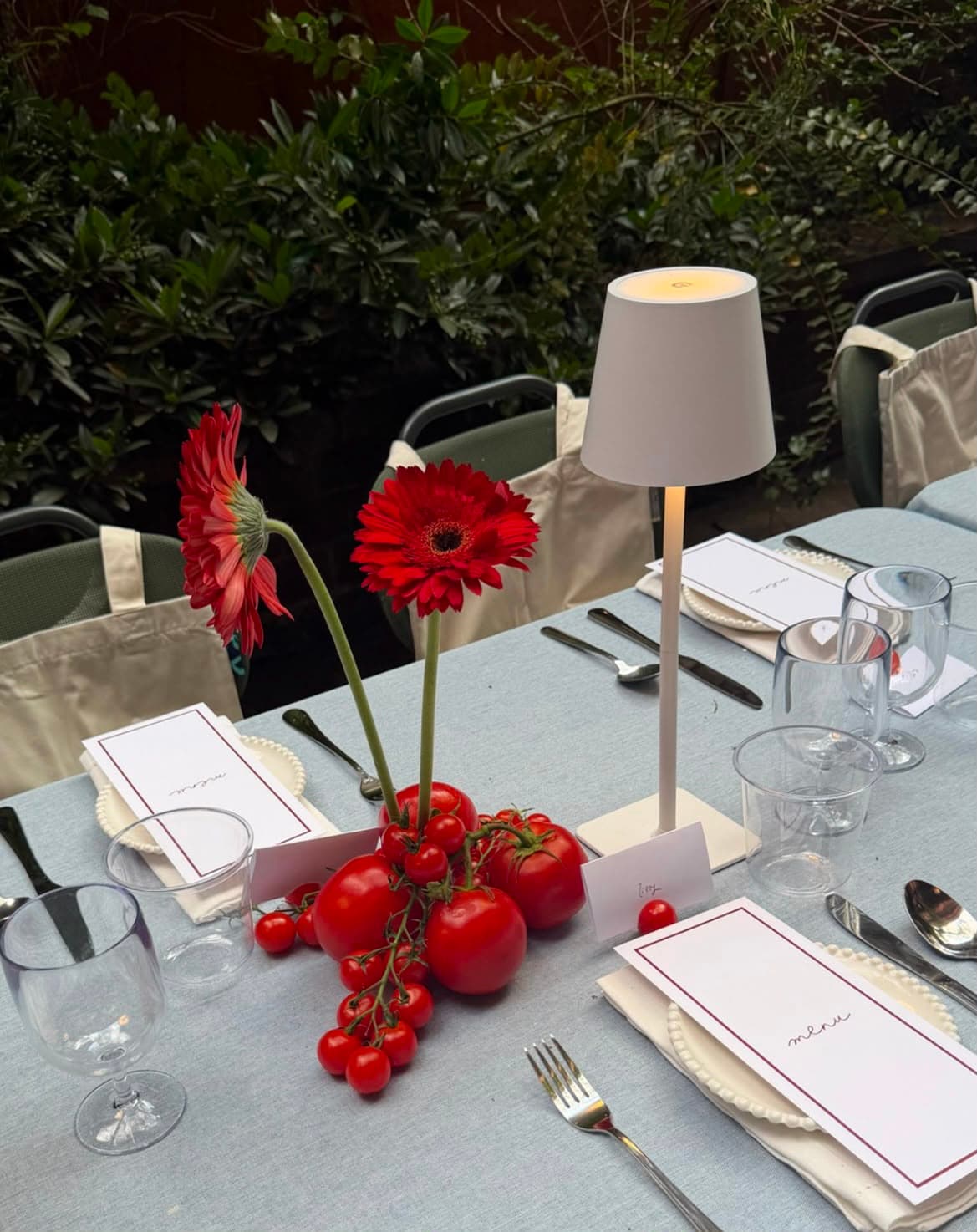An outdoor corporate event table set with candles, red florals, and menu cards