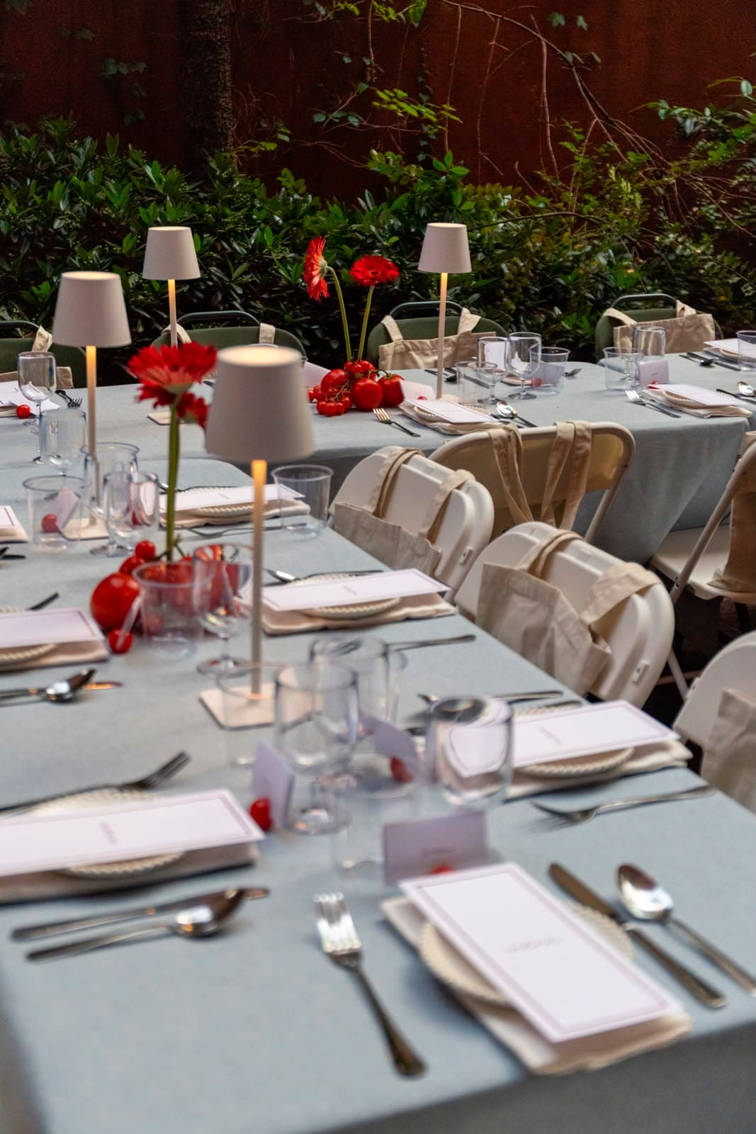 An outdoor event table set with candles and red florals